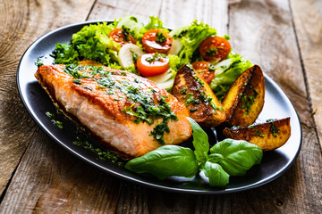 Fried salmon steak with potatoes and vegetables on wooden table