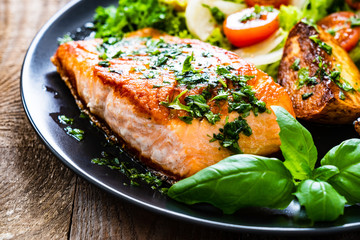 Fried salmon steak with potatoes and vegetables on wooden table