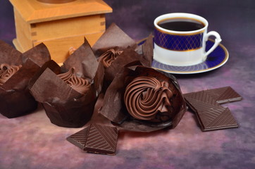 Muffin with chocolate cream, chocolate and coffee mug on colored background