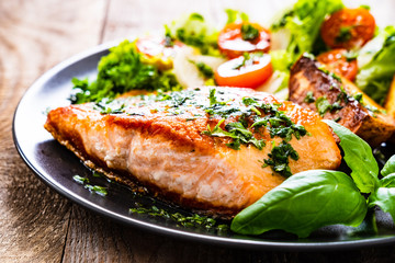 Fried salmon steak with potatoes and vegetables on wooden table