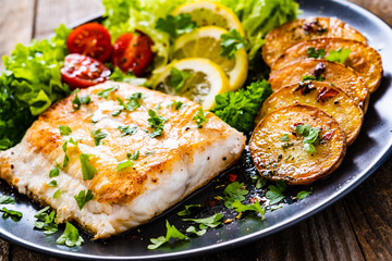 Fish dish - fried cod fillet with potatoes and vegetables on wooden table