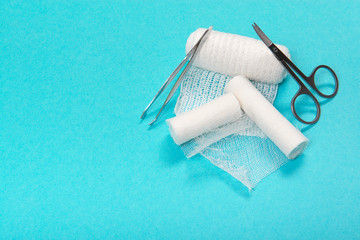 White medical bandages rolls with scissors and tweezers in a pharmacy kit on a blue background with space for copy