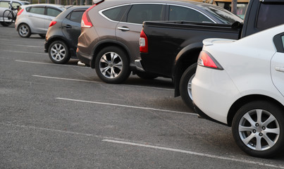 Closeup of rear, back side of white car with  other cars parking in outdoor parking area in twilight evening. 