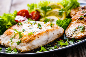Fish dish - fried cod fillet with potatoes and vegetables on wooden table