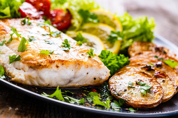 Fish dish - fried cod fillet with potatoes and vegetables on wooden table