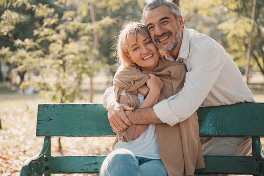 Relaxing,family,free time,age,tourism,travel and people concept.Senior couple hugging and Happy mature people in winter clothes embracing on bench.Elderly couple sitting on bench in autumn park.