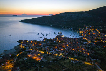 Nocturnal aerial view of seaside town of Komiza on Vis island, Croatia in Dalmatia from drone at night. Tourist destination in the Mediterranean Sea. Small city with street lights in summer at sunset.