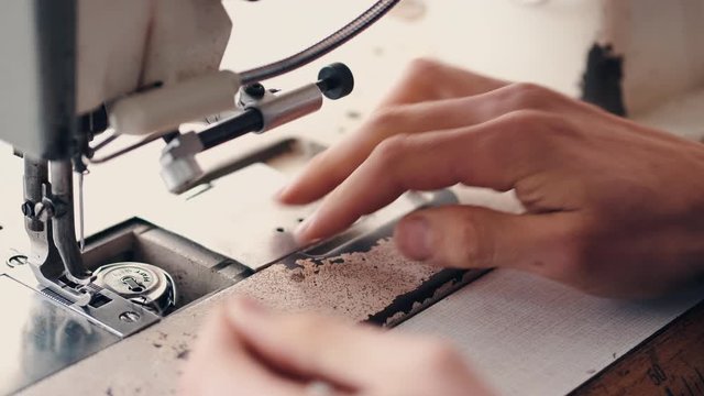 The master is preparing a sewing machine for work. The leather-dresser is putting thread through a needle.
