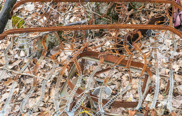 A rusty wires left on the ground, they look like parts of a bed frame. Ground is covered with dried leaves. Corrosion. Throwing rubbish into the forest.