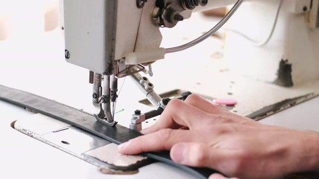 A craftsman stitches a men's leather belt on a sewing machine