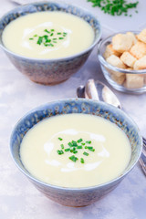 Potato leek soup in blue ceramic bowl garnished with french cream and green onion, vertical