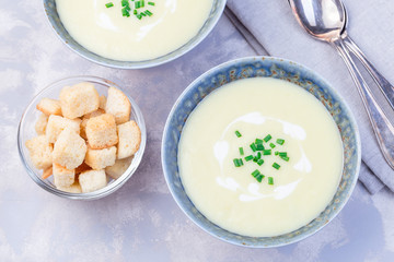Potato leek soup in blue ceramic bowl garnished with french cream and green onion, served with croutons, horizontal,  top view