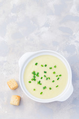 Potato leek soup in white ceramic bowl garnished with french cream and green onion, served with croutons, vertical, top view, copy space