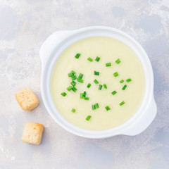 Potato leek soup in white ceramic bowl garnished with green onion, served with croutons, top view, square format