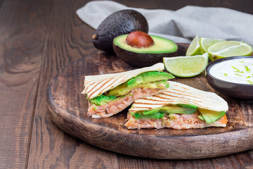 Grilled quesadilla with smoked salmon and avocado served with yogurt and lime dip, on wooden board, horizontal, copy space