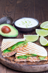 Grilled quesadilla with smoked salmon and avocado served with yogurt and lime dip, on wooden board, vertical, copy space