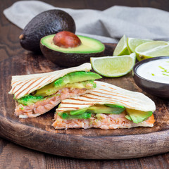 Grilled quesadilla with smoked salmon and avocado served with yogurt and lime dip, on wooden board, square format