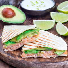 Grilled quesadilla with smoked salmon and avocado served with yogurt and lime dip, on wooden board, square format, closeup