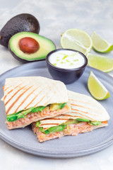 Grilled quesadilla with smoked salmon and avocado served with yogurt and lime dip, on gray plate, vertical