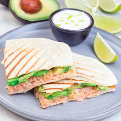 Grilled quesadilla with smoked salmon and avocado served with yogurt and lime dip, on gray plate, square format, closeup