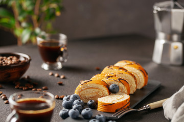 Fototapeta na wymiar Sweet roll with cream and blueberries on a board on a dark background
