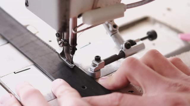 A craftsman stitches a men's leather belt on a sewing machine
