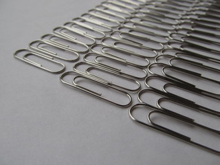 Lines of metal paper clips on a light background. Office supplies.