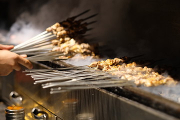 close up hand cooking mutton shashlik on barbecue grill. Traditional Chinese food. Blur background