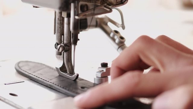 A craftsman stitches a men's leather belt on a sewing machine