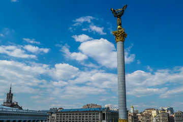 Fototapeta premium A view on Maidan Nezalezhnosti (Independence Square) in Kiev. In the center there is the Victory column with Statue of Berehynia on top of it. A woman is holding golden branch. Clear and blue sky.