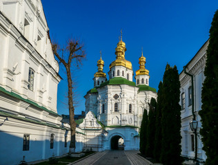 A distanced view on Pechersk Lavra in Kiev, Ukraine, known as the Kiev Monastery of the Caves. It is a historic Orthodox Christian monastery. Green rooftops with golden domes. Walls are painted white.