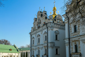 A close-up view on Pechersk Lavra in Kiev, Ukraine, known as the Kiev Monastery of the Caves. It is a historic Orthodox Christian monastery. Green rooftops with golden domes. Walls are painted white.