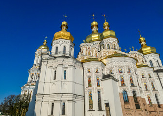 Fototapeta na wymiar A close-up view on Pechersk Lavra in Kiev, Ukraine, known as the Kiev Monastery of the Caves. It is a historic Orthodox Christian monastery. Green rooftops with golden domes. Walls are painted white.
