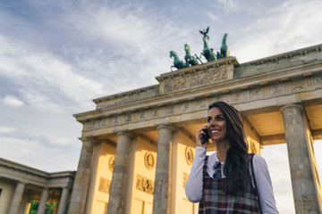 Smiling cool and young woman talking on a mobile phone in Brandenburg Gate in Berlin, Germany.