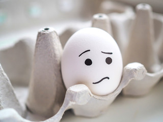 Lonely egg with sad emoji lies in a box