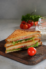 Cheese sandwich of toasted bread with a crispy crust with fresh tomatoes and herbs on a wooden board
