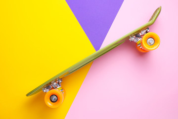 Green skateboard with orange wheels on yellow,purple and pink background. Plastic mini cruiser...