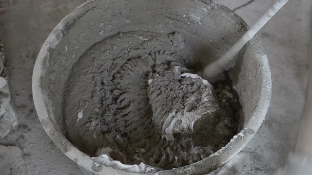 Mixing cement for construction in a small black tank. Worker mixing plaster in a bucket. Worker mixes a solution in a black bucket.