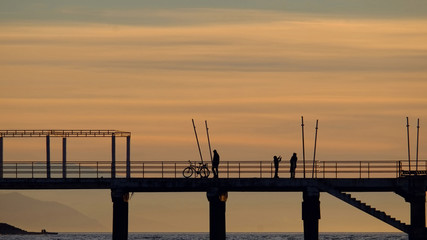 Fototapeta na wymiar Silhouettes of the people on the pier with sunset sky background