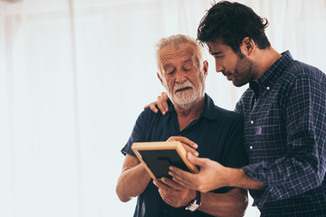 Sweet bonding. Cheerful elderly man sitting on the sofa next to his adult son, hugging him and...