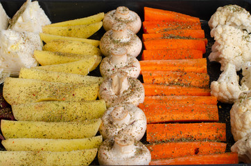 Uncooked vegetables on baking sheet. Potatoes, field mushrooms, carrots, cauliflower.