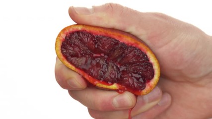 Close-up of unrecognizable man squeezing half of ripe juicy blood orange. Fresh citrus juice dropping down. Isolated, on white background