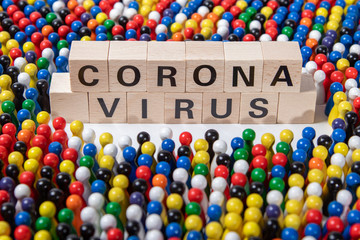 corona virus text on wooden cubes, surrounded by wooden figurines in several colours
