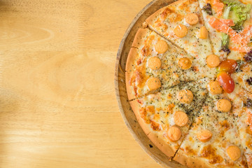 Cutted crust italian sausage and bacon pizza with mozzarella cheese in the wooden pan on the wooden table. Top view of homemade pizza with ingredients. It's junk food and unhealthy food