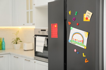 Modern refrigerator with child's drawing, notes and magnets in kitchen. Space for text