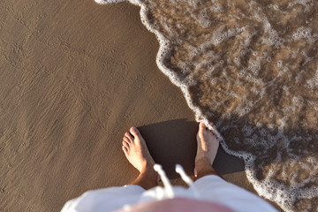 View from above on only bare feet. Anonymous legs, standing on sea shore. Sun light, beach, sand...