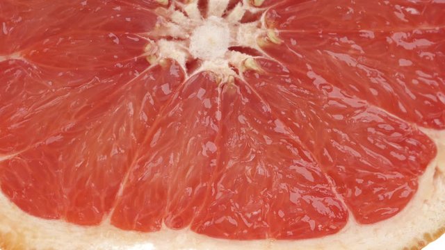 Macro shot of a slice ripe juicy grapefruit being rolled and squeezed. Fresh citrus juice dropping down. Isolated, on white background