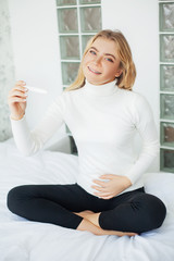 Woman with pregnancy test in bright white room