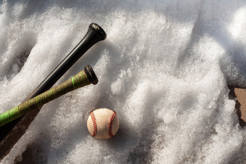 Spring baseball.  baseball bat laying in the snow with baseball.  Snow melting on baseball field