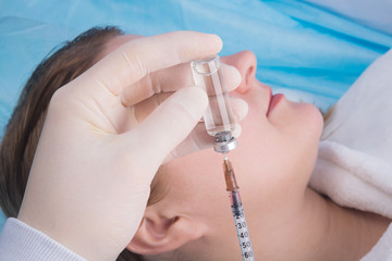 doctor in protective gloves, typing in a syringe, a drug for injection, on the background of the patient, close-up